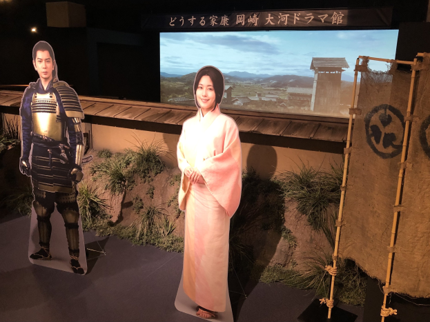 Eine Frau in einem pinken Kimono und ein Mann in einem Samurai-Kostüm, die gemeinsam in einer Szene aus einem japanischen Film lächeln.