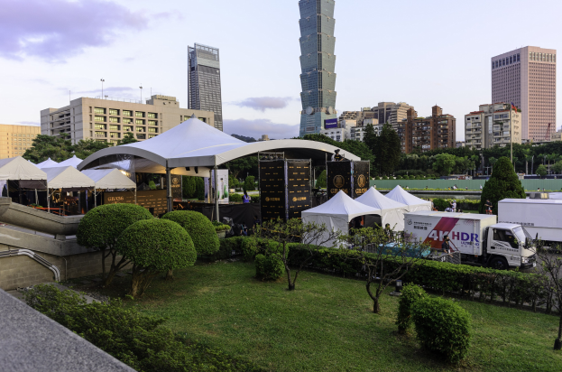 Eine Gruppe von Zelten in einem Park mit grünem Bereich, Menschen, Fahrzeugen, Gebäuden und einem klaren Himmel, wahrscheinlich während des Hong Kong International Film Festivals.
