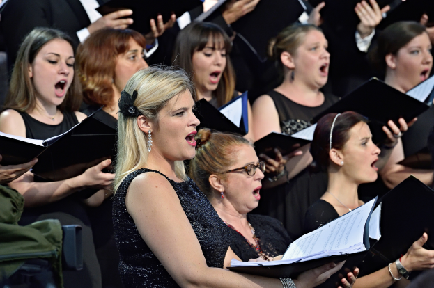 Eine Gruppe von Frauen, die in einem Chor singen, einige halten Bücher in den Händen, mit einer Person im Vordergrund und einem unscharfen Hintergrund.
