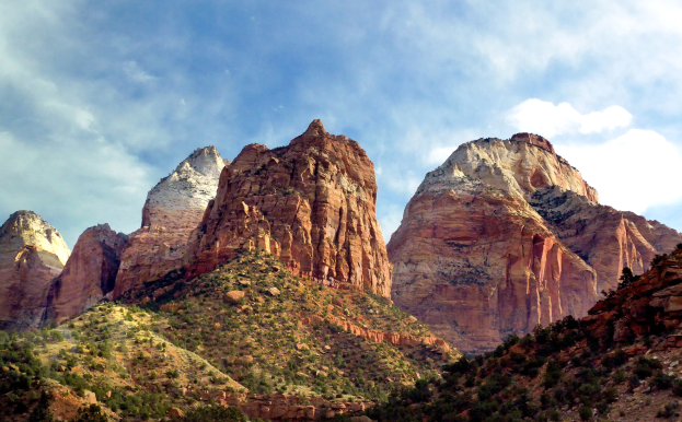 Zion Nationalpark in Utah mit majestätischen Bergen, grünen Bäumen, steinigem Gelände und weißen Wolken am Himmel.