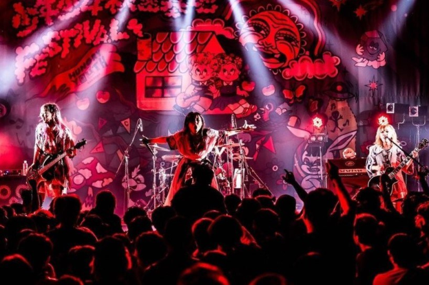 Ein Live-Auftritt der japanischen Rockband Korn auf der Bühne mit Musikern, die Gitarren spielen und singen, begleitet von Mikrofonen und Ständern, während das Publikum unten zusieht.