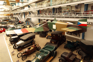 Eine große Museumsausstellung mit verschiedenen Oldtimern, Flugzeugen, Fahrrädern und Informationsschildern, bei der Besucher die Ausstellungsstücke betrachten.