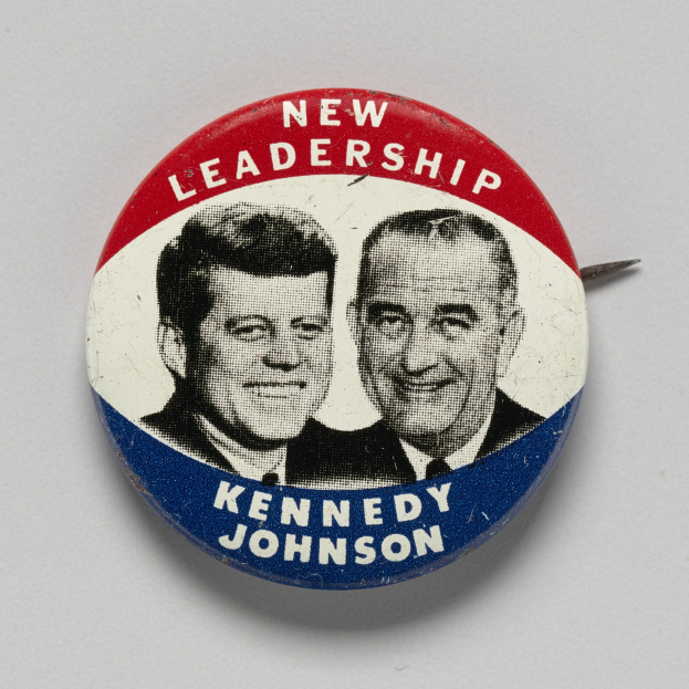 Ein Ansteckbutton auf einer weißen Oberfläche zeigt zwei Bilder von Kennedy und Johnson mit dem Text "New Leadership" darunter.