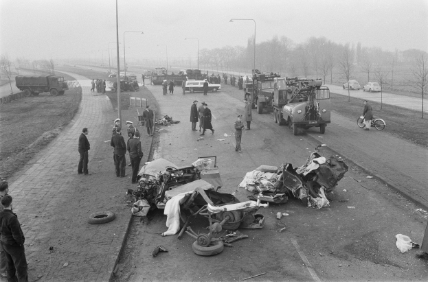 Schwarze und Weiße Szenerie eines Autounfalls am Straßenrand mit mehreren Fahrzeugen, einer Gruppe von Menschen in der Nähe, Laternenpfählen, Bäumen und dem Himmel im Hintergrund.