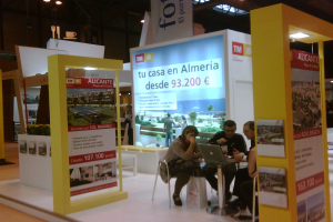 Eine Gruppe von Menschen, die um einen Tisch herum auf Stühlen sitzen und auf einen Laptop schauen und arbeiten, mit mehreren Flyern, auf denen verschiedene Werbeanzeigen zu sehen sind.