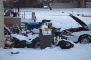 Eine Außenszene mit Mülll im Zentrum, einem Auto auf der rechten Seite, Treppen auf der linken Seite, Bäumen oben und Eis am Boden.