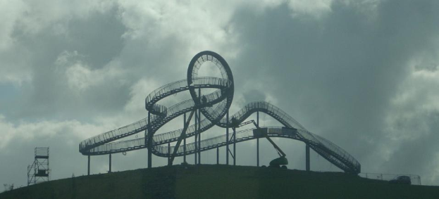Eine Achterbahn auf dem Höhepunkt eines Hügels mit einem bewölkten Himmel im Hintergrund, umgeben von Stützpfählen und -strukturen.