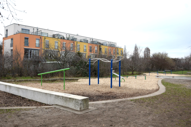 Spielplatz mit einem Gebäude, Bäumen und einem klaren blauen Himmel über grünem Gras.