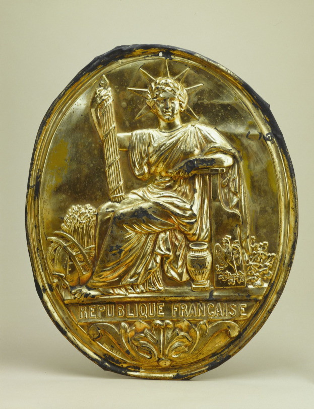 Goldenes rundes Schild mit erhabener Statue of Liberty-Gestaltung und eingraviertem Text, vor einem weißen Hintergrund.