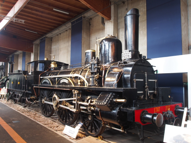 Alte Dampflokomotive im Museum ausgestellt, umgeben von Eisenbahnschienen und Informationsschildern.