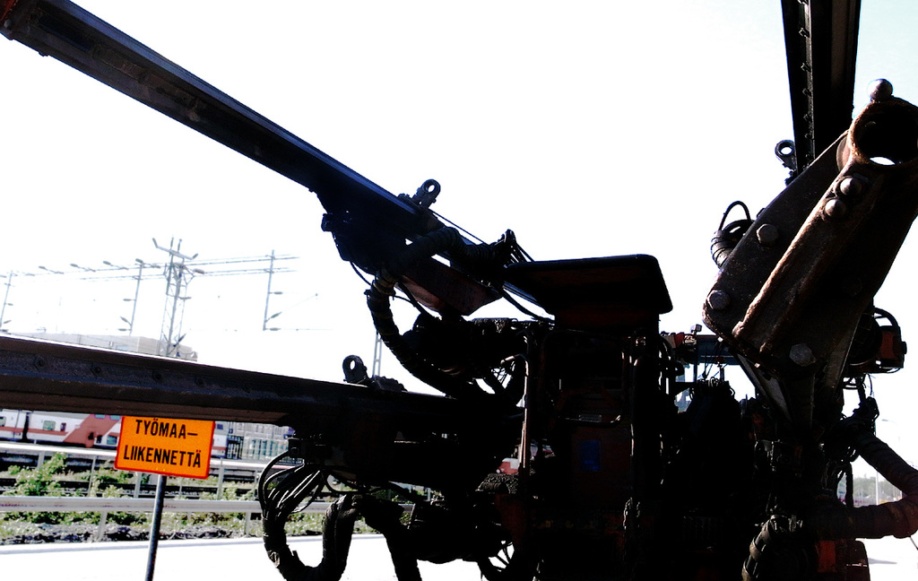 Eine Maschine ist im Vordergrund mit Strommasten, Kabeln, Absperrungen, Pflanzen und Himmel im Hintergrund.